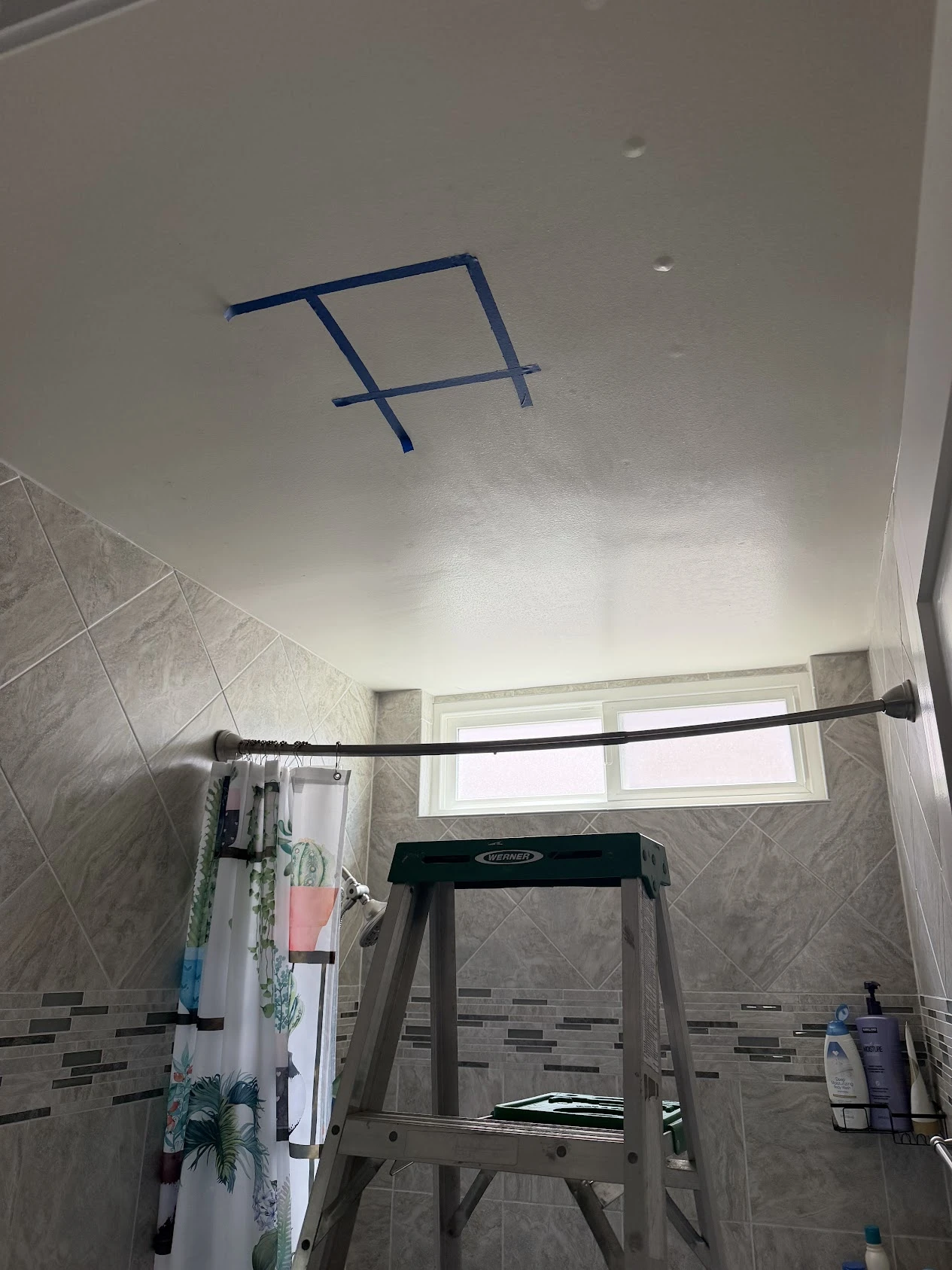 Original project photo: blue tape marking a square on the bathroom ceiling, with a ladder below